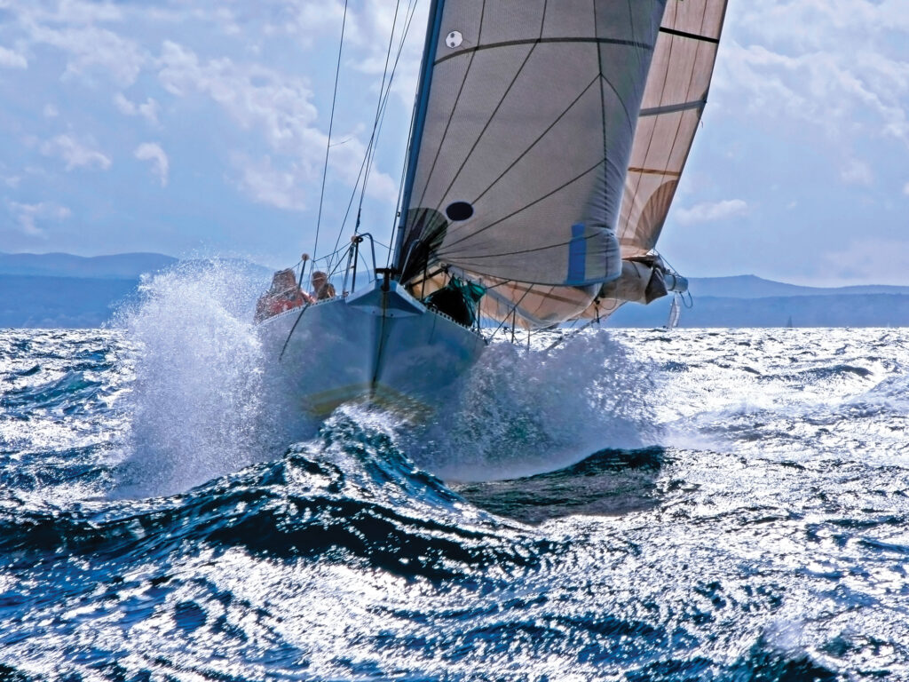 Sailboat breaking with the prow through the splashing wave on the rough sea