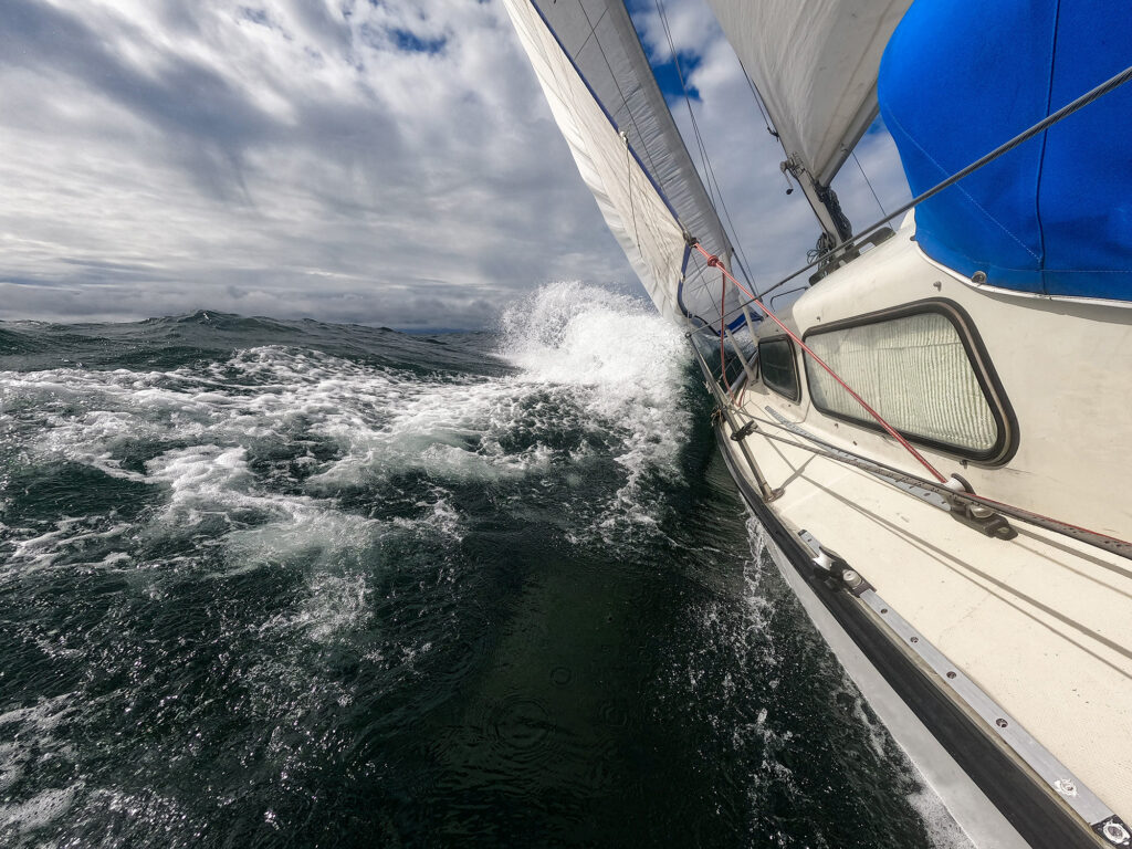 Sailboat fights storm and waves in open sea.