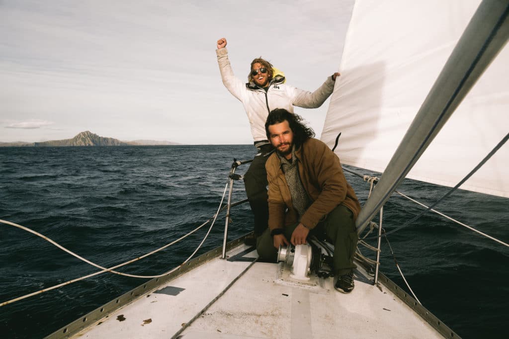 Two guys standing on a sailboat in the water.